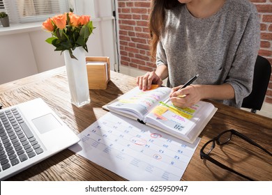 Close-up Of A Businesswoman Making Agenda On Personal Organizer At Workplace