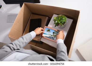 Close-up Of A Businesswoman Packing Picture Frame In Cardboard Box At Workplace