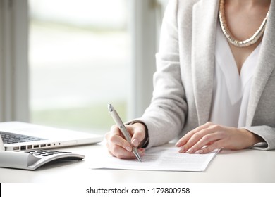 Close-up of businesswoman sitting at desk and fill the form. 