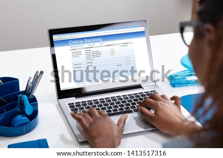 Close-up Of A Businesswoman's Hand Doing Online Banking On Laptop Over White Desk