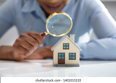 Close-up Of A Businesswoman's Hand Holding Magnifying Glass Over House Model Over Desk