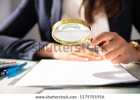 Close-up Of A Businesswoman's Hand Looking At Contract Form Through Magnifying Glass