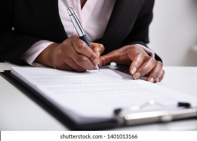 Close-up Of Businesswoman's Hand Signing On Papers Over Desk