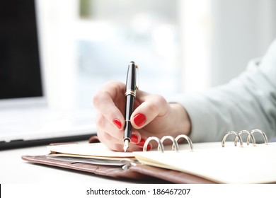 Close-up of businesswoman's hand while writing note in diary. Small business.