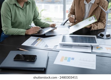 Close-up of businesswomen working sitting together at workplace, discussing  about strategies, plans, analytic progress, and financial stats, and pointing at graph documents on desk with files.  - Powered by Shutterstock