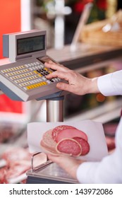 Closeup Of Butcher Holding Cold Cuts While Pressing Button On Weighing Scale In Shop