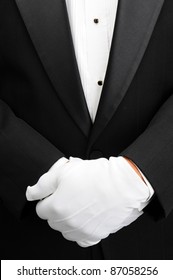 Closeup of a butler with his white gloved hands in front of his body. Man is wearing a tuxedo showing only his torso in vertical format.