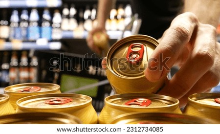 Close-up of a buyer hands taking two beautiful golden cans of beer and putting them into a shopping trolley