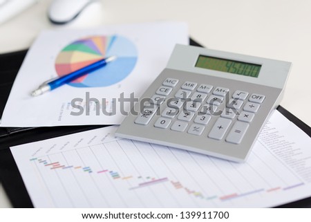 Closeup of calculator; diagrams drawn on papers at desk