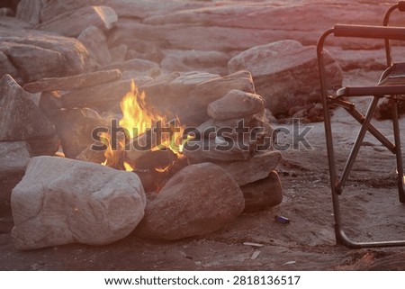 Close-up of a campfire burning in a stone fire pit beside the ocean in eastern Canada. Cozy outdoor scene featuring glowing flames, rugged coastline and the peaceful atmosphere of a seaside campsite.