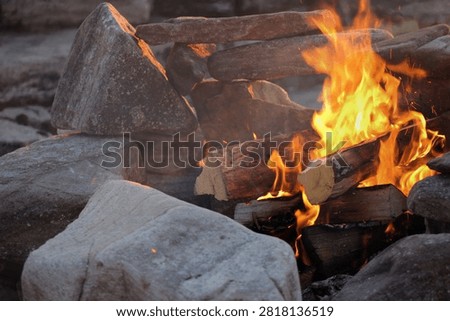 Close-up of a campfire burning in a stone fire pit beside the ocean in eastern Canada. Cozy outdoor scene featuring glowing flames, rugged coastline and the peaceful atmosphere of a seaside campsite.