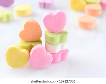 Closeup of candy Valentines hearts on a white reflective surface. Horizontal format with out of focus candies in the background.