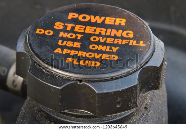 Closeup of a cap of a\
power steering oil tank. Do not overfill and use approved fluid\
only warning text.