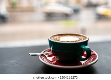 Close-up of a cappuccino cup with heart-shaped latte art on a saucer with a spoon, set against a blurred street view background. Perfect for themes of coffee, relaxation, and urban lifestyle. - Powered by Shutterstock