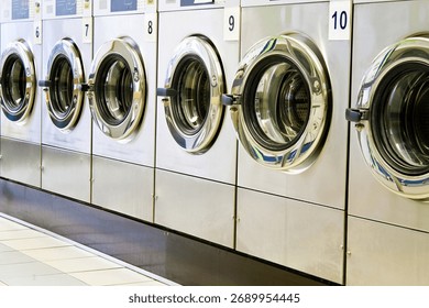 A close-up caption from a diagonal view of metallic lustered clothes washer’s in a public launderette. Horizontal shot, image taken with a full frame camera and a prime lens at daylight.