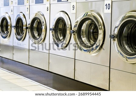 A close-up caption from a diagonal view of metallic lustered clothes washer’s in a public launderette. Horizontal shot, image taken with a full frame camera and a prime lens at daylight.