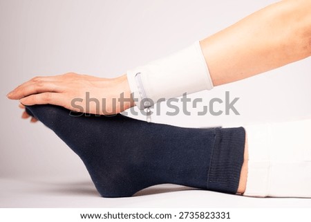 A close-up captures a hand pressing on a foot in a navy blue sock during a stretch, with a white zippered wristband visible, focusing on functional fitness and lifestyle