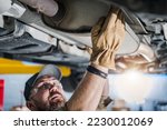 Closeup of Car Catalytic Converter Being Checked by Professional Mechanic at Vehicle Repair Station. Bottom View. Automotive Theme.