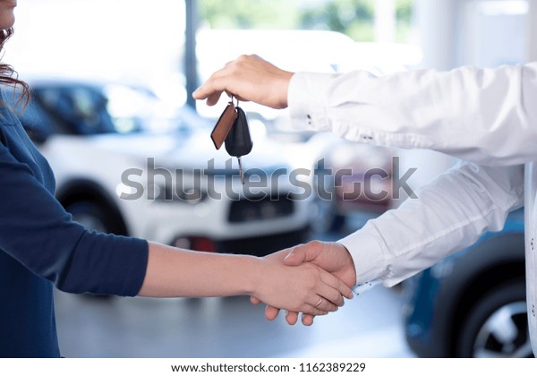 Close-up of car dealer shaking buyer\'s hand\
and giving keys after\
transaction