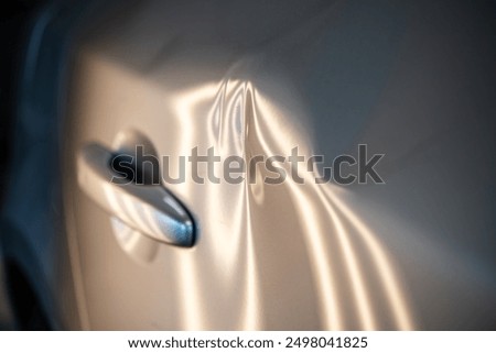 Close-up of a car door featuring multiple dents illuminated by soft lighting, illustrating the effects of minor accidents. Essential for insurance claims and automotive repair services