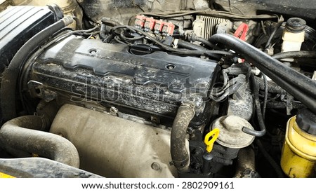 Close-up of a car engine with visible components, hoses, and wires. Showing signs of wear and dirt, perfect for automotive repair or maintenance visuals.