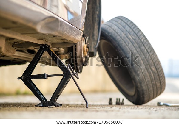 Closeup of a car\
lifted on jack in process of new wheel tire replacement. Breakdown\
of a vehicle on a\
street.