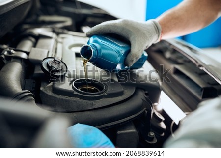 Close-up of car mechanic changing engine oil while working in a workshop. 