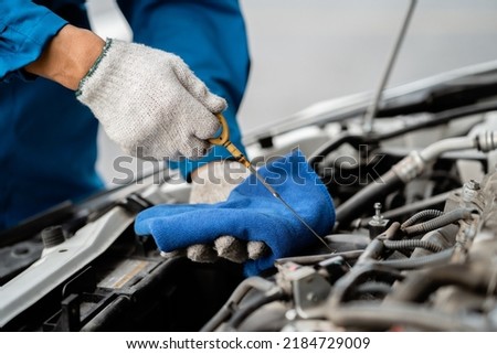 Close-up, a car mechanic checking the oil in a car's engine. Technician inspecting and maintaining the engine of a car or vehicle. Female car mechanic checking car engine