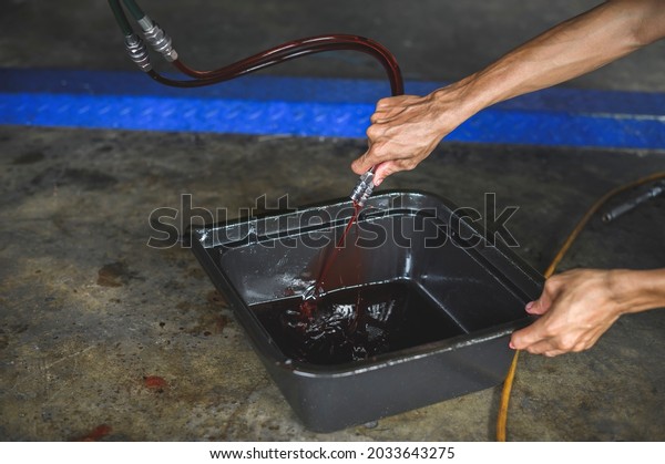 Close-up of Car mechanic hands\
pouring old used automatic transmission fluid into the oil drain\
pan.