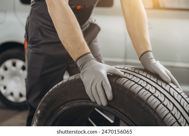 Close-up Car Mechanic holding a tire at the repair garage. Replacement of winter and summer tires - Powered by Shutterstock