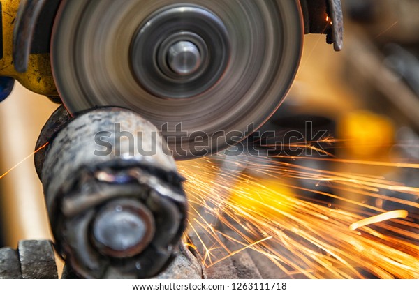 A close-up\
of a car mechanic using a metal grinder to cut a car silent block\
in an auto repair shop, bright flashes flying in different\
directions. Work of auto\
mechanics.