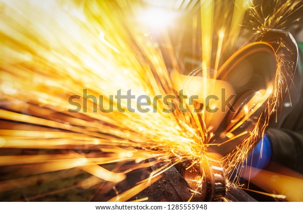 A close-up of a car\
mechanic using a metal grinder to cut   bearing in an auto repair\
shop, bright flashes flying in different directions. Work of auto\
mechanics.