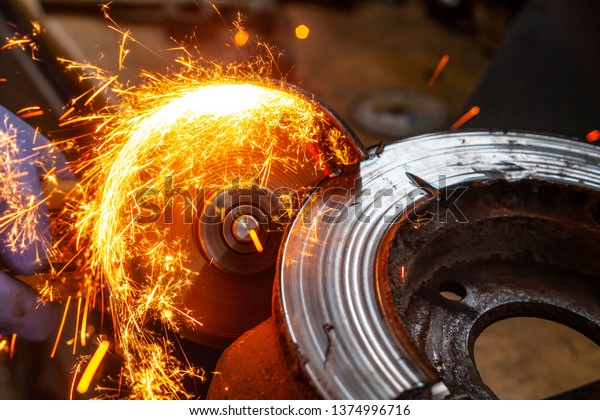 A\
close-up of a car mechanic using a metal grinder to cut a brake\
disk  in an auto repair shop, bright flashes flying in different\
directions, in the background tools for an auto\
repair