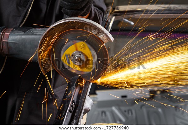 A close-up of a car mechanic using a metal grinder\
to cut a car silent block in a vise in an auto repair shop, bright\
flashes flying in different directions, in the background tools for\
an auto repair