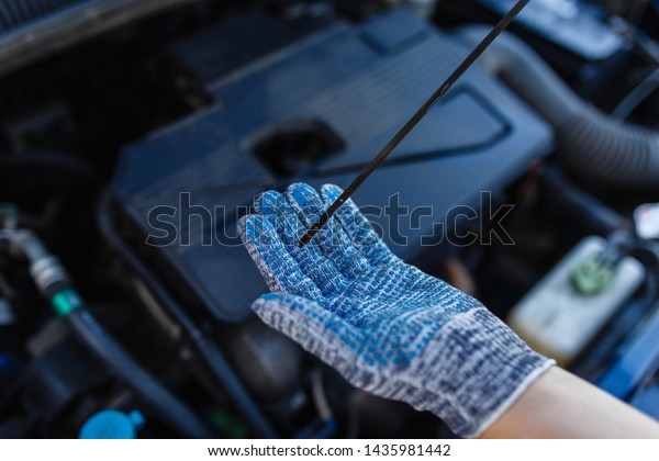 Close-up car\
mechanic\'s hands in gray gloves holding dipstick of oil level in\
the engine. Auto mechanic checks oil level in car engine with\
finger pointing the correct oil\
level.