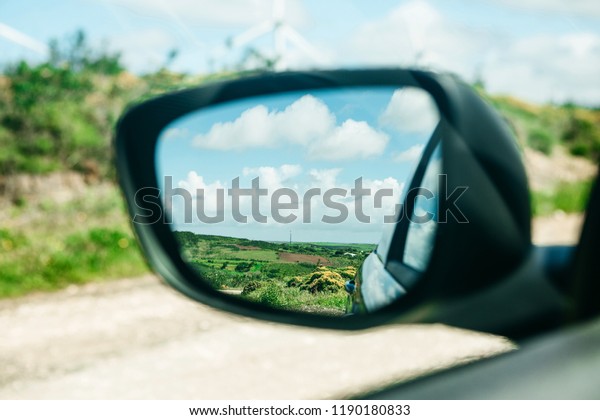 Close-up of a\
car rear view mirror in which a beautiful blue sky and a rural\
landscape. Traveling in the\
countryside.