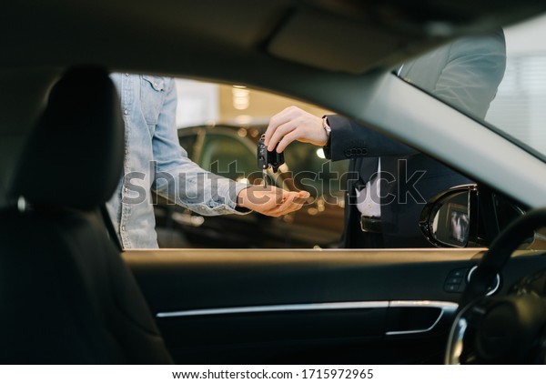 Close-up of car salesman\
handing over keys for new car to young man buyer in auto\
dealership, view from interior of car. Concept of choosing and\
buying new car at\
showroom.