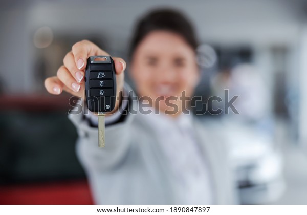 Closeup of car seller holding and\
handing a car keys towards camera while standing in car\
salon.