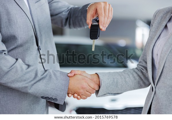 Closeup of car seller\
shaking hands with customer and handing her car keys while standing\
in car salon.
