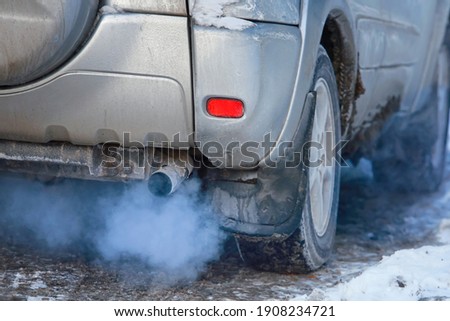 Close-up of car smoking exhaust pipe, car with gasoline engine. Gasoline engine warming up at idle in winter season. Blue exhaust smoke