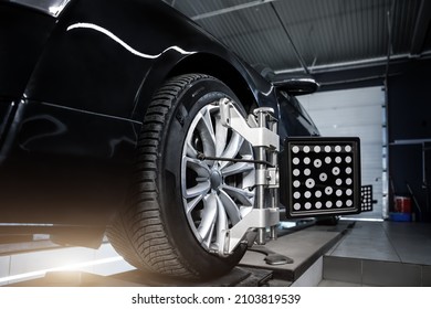 CLose-up car wheel indoors service maintenance repair center against laser sensor equipment diagnostics and 3d wheel alignment. Vehicle inside garage workshop for auto camber toe check fixing work - Shutterstock ID 2103819539
