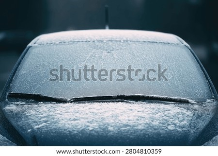 Close-up of a car windshield completely covered in a thick layer of ice and snow, with wipers visible beneath the frost.