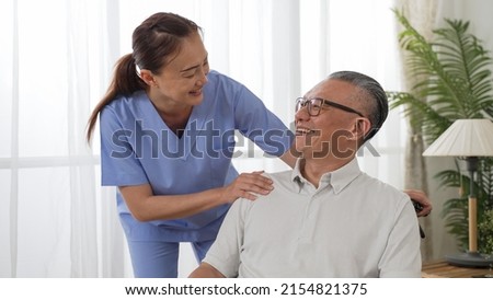 Closeup of caring Asian woman nursing aide talking and encouraging older male patient during home visit. Domiciliary care for elderly senior concept