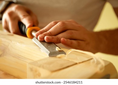 A close-up of a carpenter hands skillfully using a chisel on a wooden board. The focus is on the detailed work, with the wood grain visible and the chisel carving into the surface.