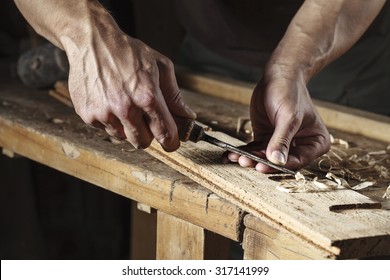 Closeup of a carpenter hands working with a chisel and carving tools on wooden workbench
