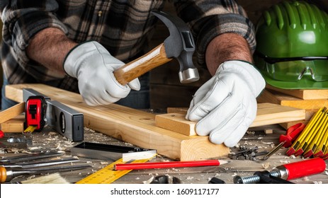Close-up. Carpenter with his hands protected by gloves, with hammer and nails fixes a wooden board. Construction industry, do it yourself. Wooden work table.