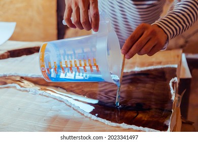 Closeup Of Carpenter Pouring Epoxy Liquid In A Wooden Table. Process Of Making A Craft Resin And Wood Table