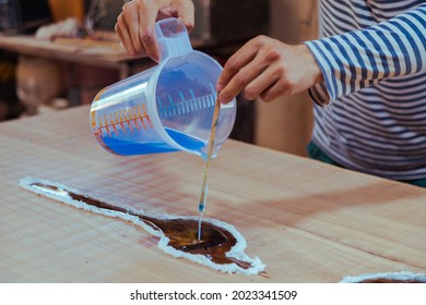 Closeup Of Carpenter Pouring Epoxy Liquid In A Wooden Table. Process Of Making A Craft Resin And Wood Table