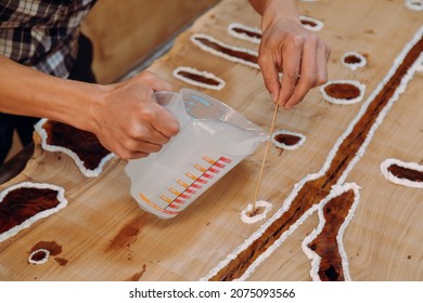 Closeup Of Carpenter Pouring Epoxy Liquid In A Wooden Table. Process Of Making A Craft Resin And Wood Table