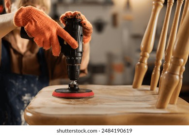 Close-up of a carpenter sanding a chair with a wood sander. production and restoration of furniture - Powered by Shutterstock